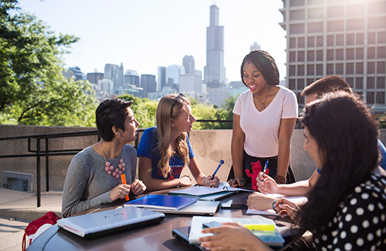 a group of students appearing to study together in one of U I C's outdoor spaces with the Chicago skyline in the background.